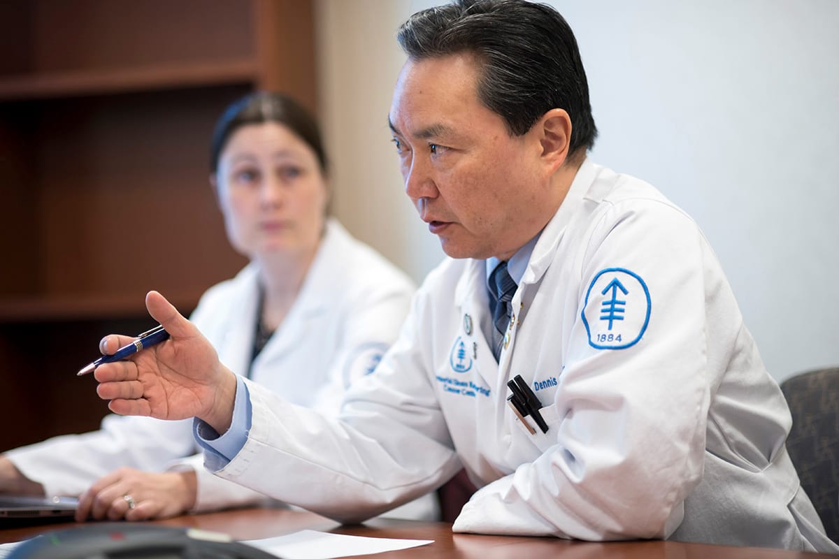 MSK Surgeon in white lab coat sitting in profile (facing left) talking and gesturing.