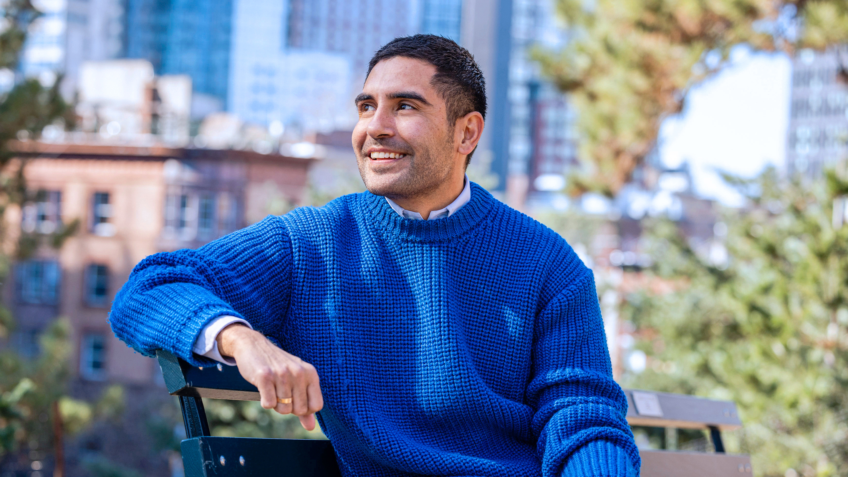 A young man who was treated for colorectal cancer at MSK smiles as he sits on a park bench.