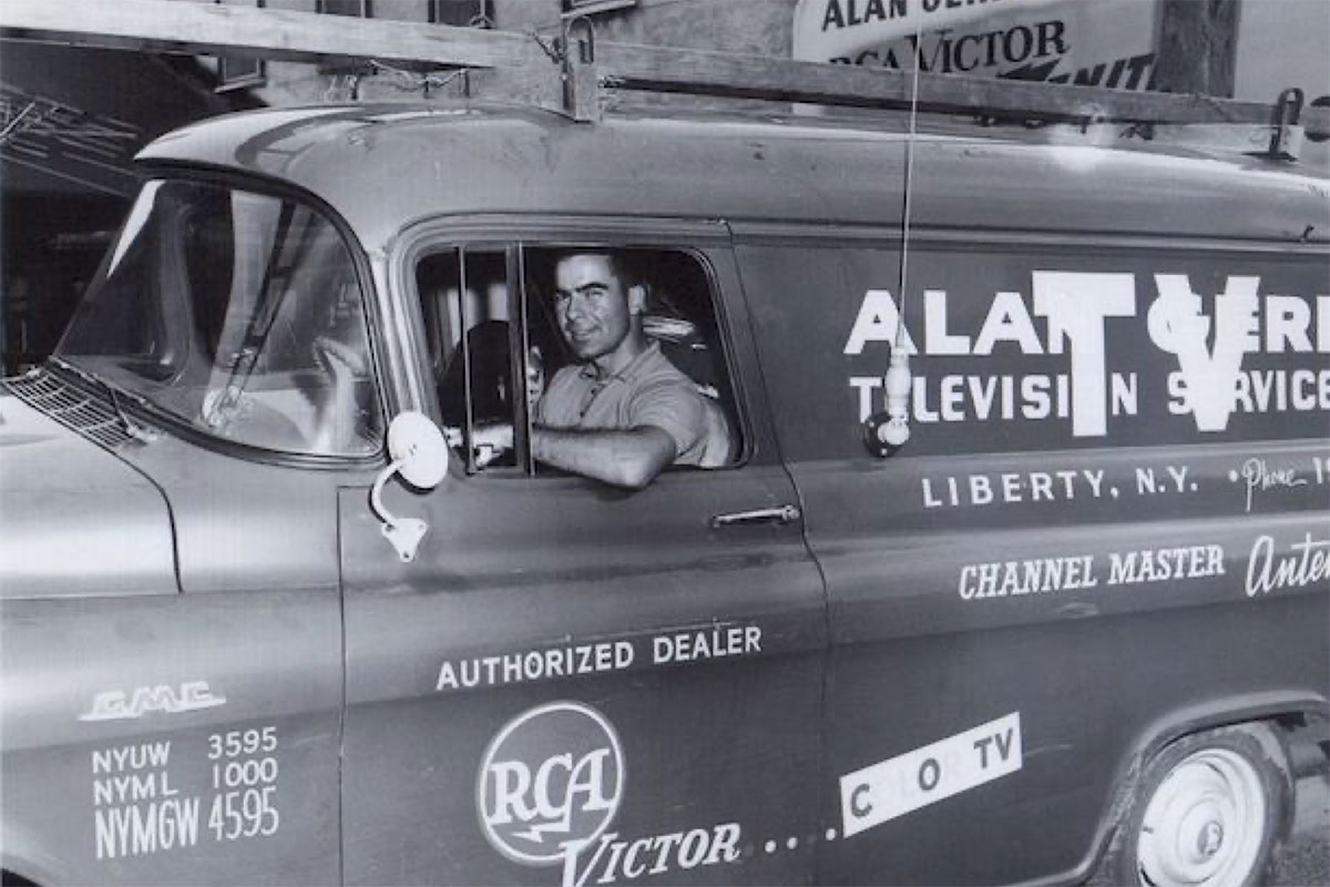 A black and white photo of Alan Gerry in a tv repair truck.