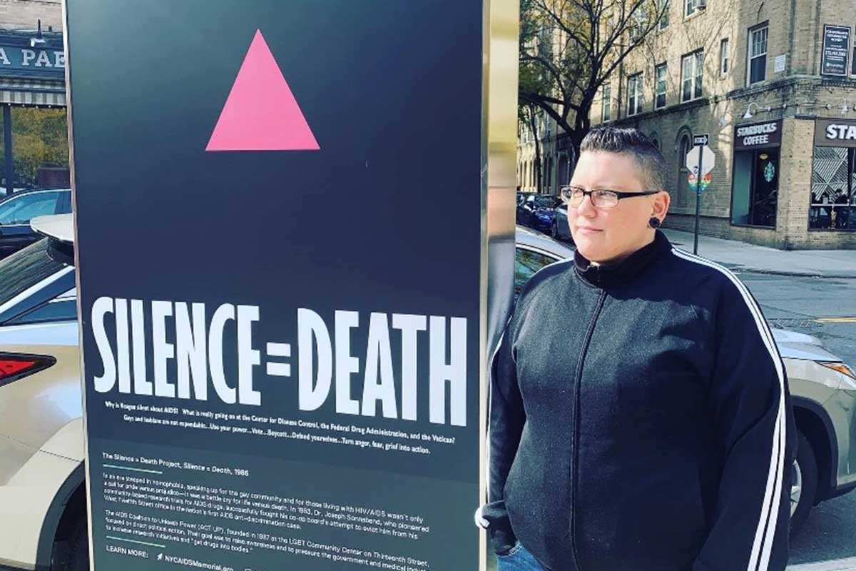 Nikki in New York City, standing next to a poster designed in the late ’80s by the Silence=Death Project to raise awareness for the AIDS crisis.