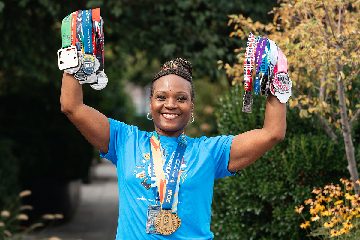 Breast cancer patient LaDawn Jefferson holds up her running medals joyfully  