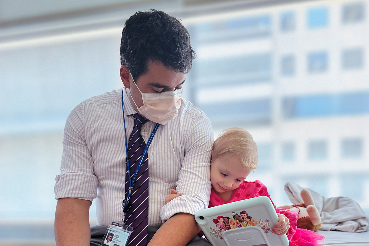 Dr. Michael Ortiz and Sienna sit on a hospital bed together looking at a tablet