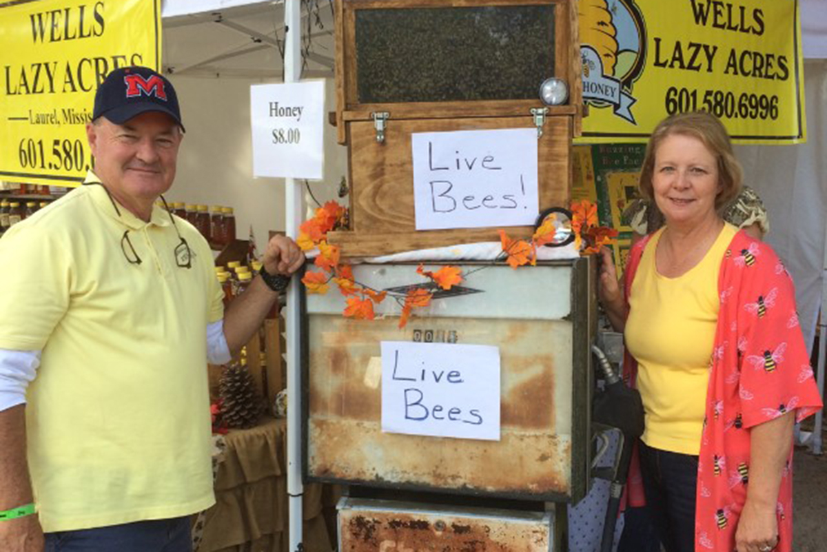 Man and woman in front of bee colony booth.