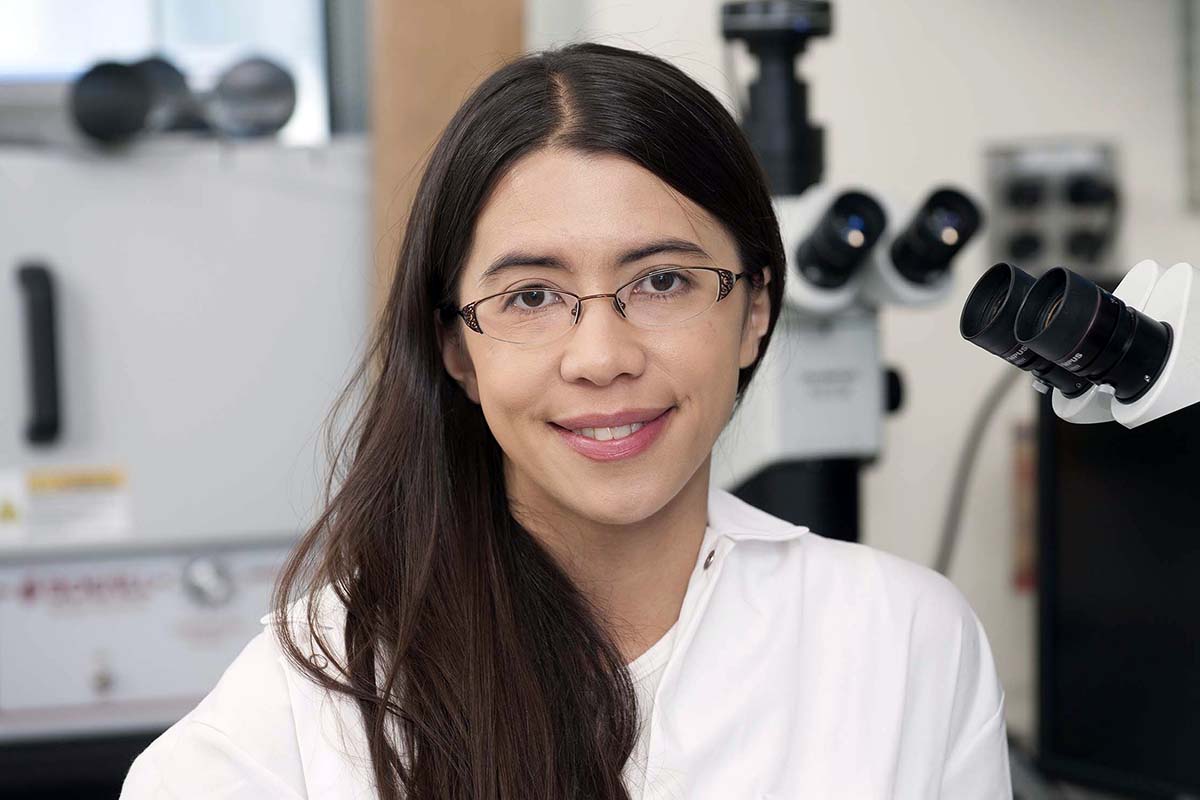 PhD Elizabeth Wasmuth poses smiling beside a microscope.