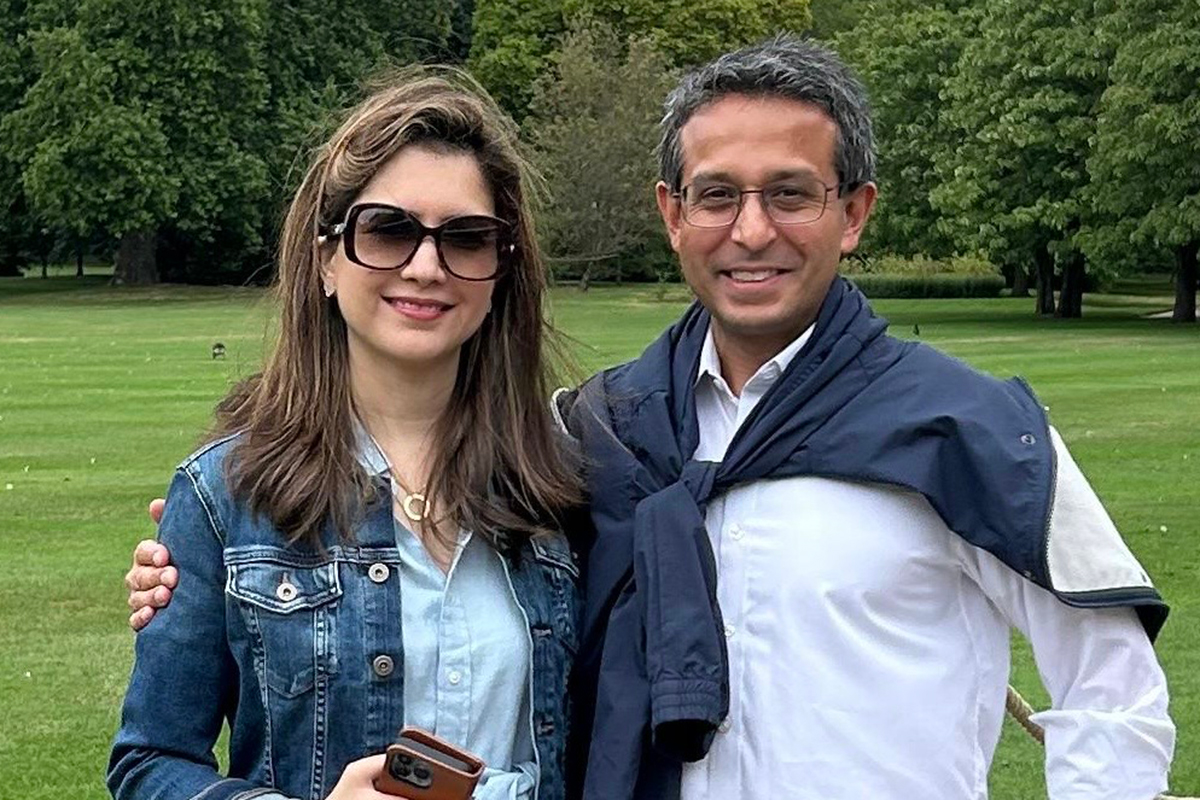 Man and woman smiling with park in background.