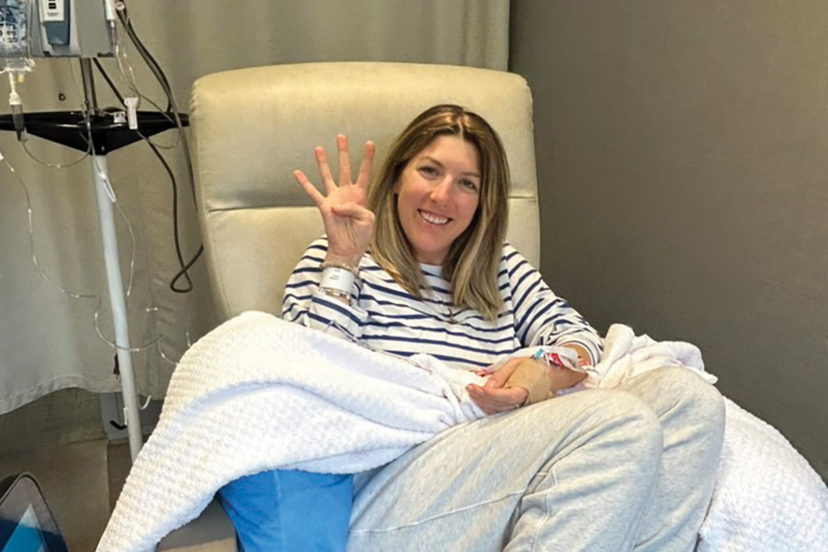 Woman in chemotherapy chair holding up four fingers.