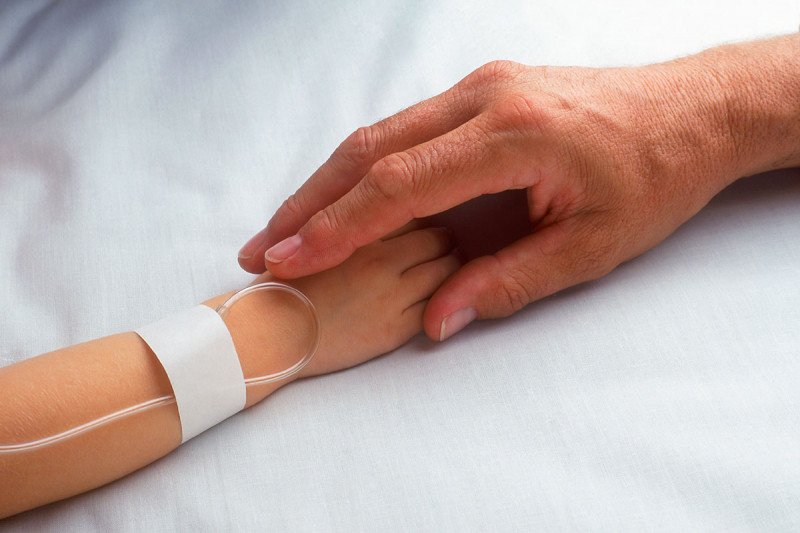 Child hand with IV holding adult hand.