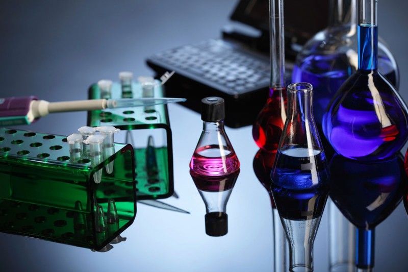 Test tubes and glass vials and beakers sit on a desk in a laboratory.