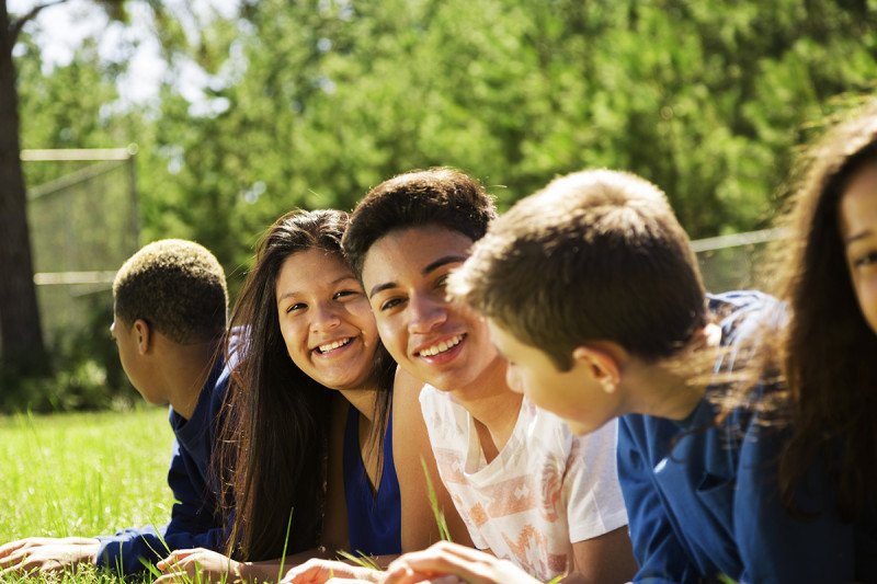 Group of racially diverse boys and girls lying on grass and conversing.