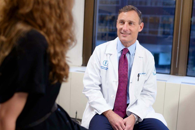 Emmanuel Pappou, cirujano de MSK, sonríe a la cámara en su uniforme médico.