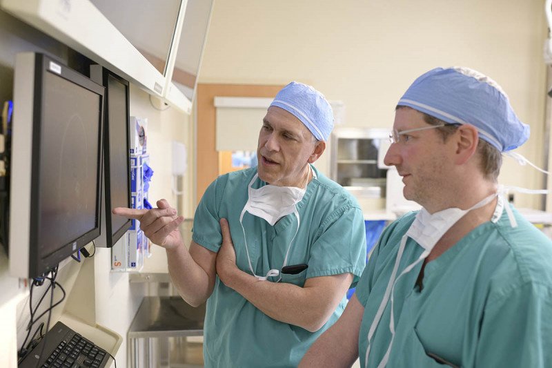 MSK acoustic neuroma experts Samuel Selesnick (left) and Cameron Brennan (right) dressed in their scrubs looking at a computer screen.