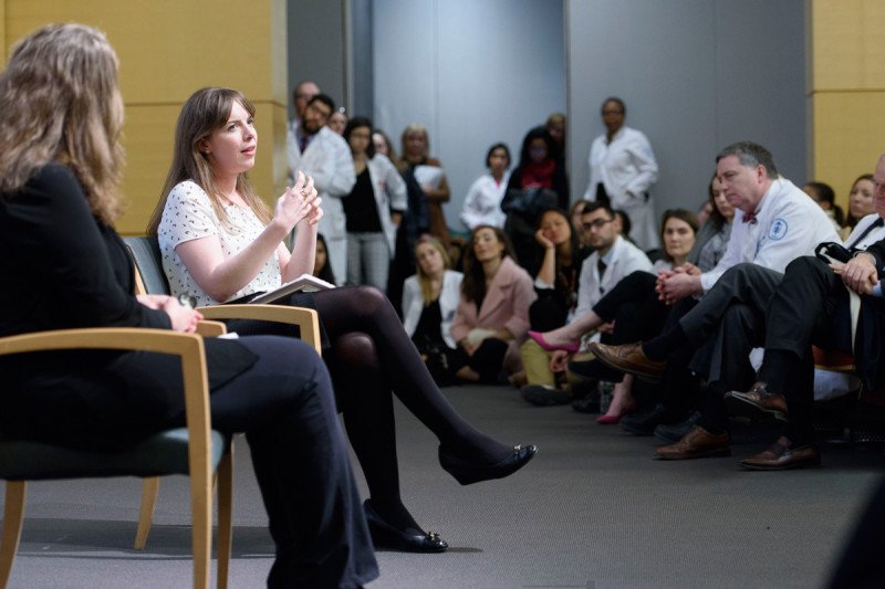 Lucy Kalanithi gestures while speaking. Physicians in white lab coats look on.