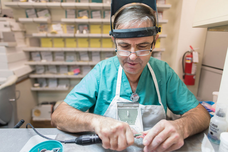 Man with glasses holding a dental prosthetic and tools in his hands.