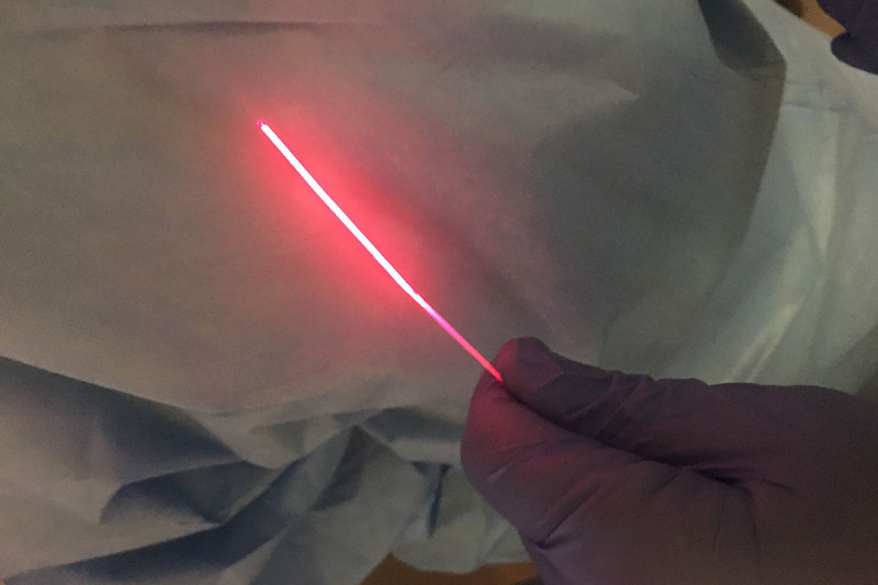 A hand holding a thin optical fiber giving off a red light.