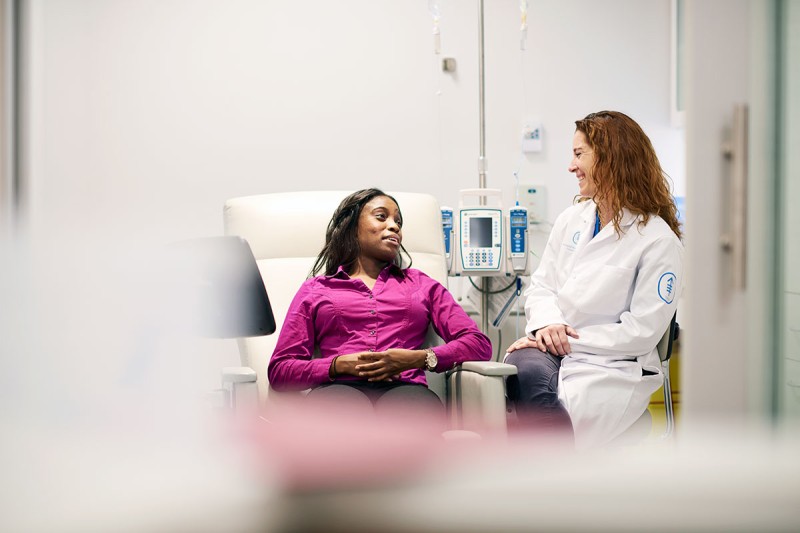 Patient on left in chemotherapy infusion chair talking to nurse