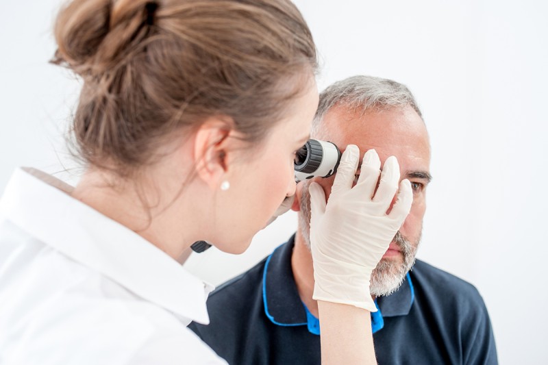 Dermatologist examining skin on the face of older man.