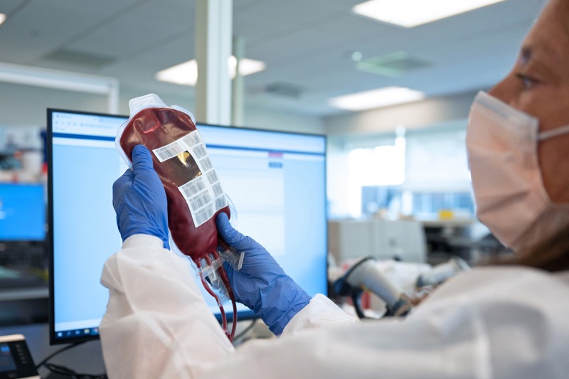 A person wearing a mask and gloves holds a bag of cord blood.