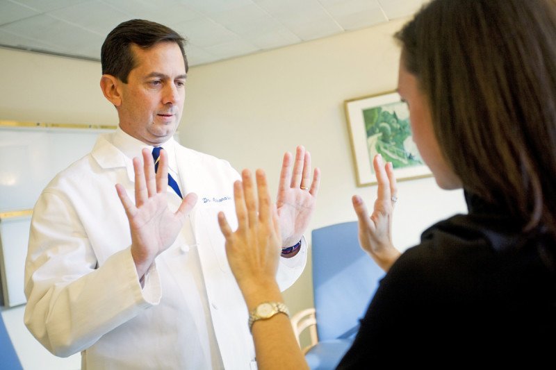 MSK surgeon, Edward Athanasian, examining a female patient by holding both of their hands in the air. 