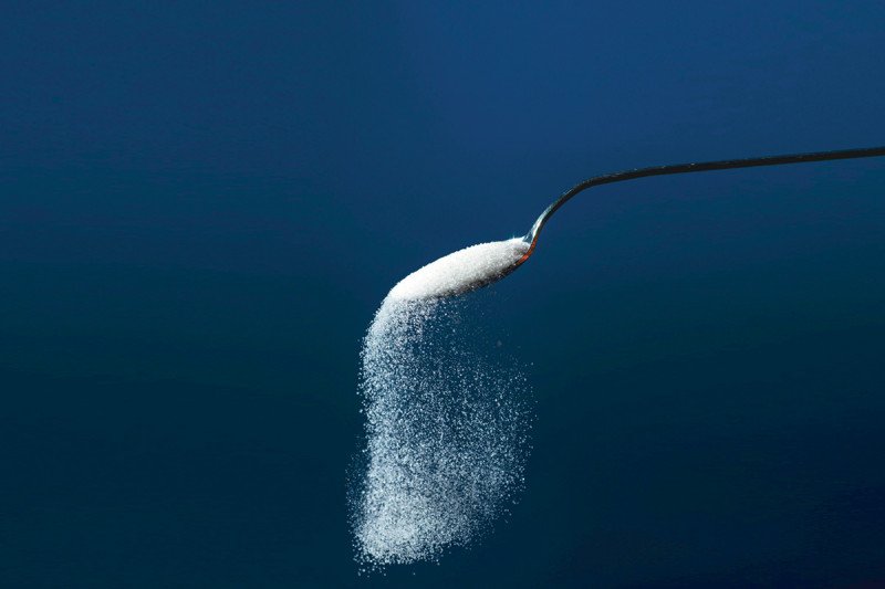 Sugar pouring out of a spoon on a blue background