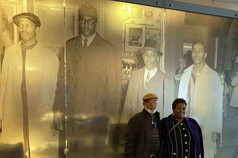 Dr. Smith’s parents, Arthur and Barbara Smith, in front of a photograph of the Greensboro Four protest in 1960. Barbara’s Smith cousin, Joseph McNeil (far right), is one of the members of the Greensboro Four