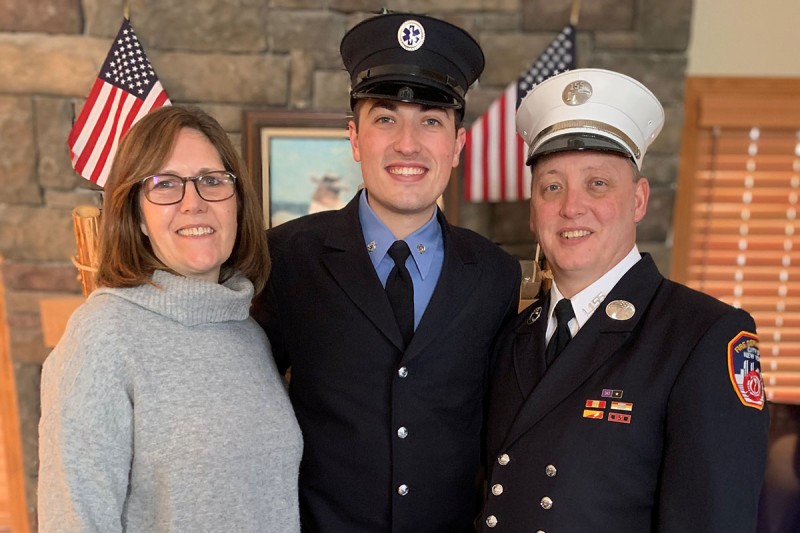 Woman pictured with son in EMT uniform and husband in firefighter uniform. 