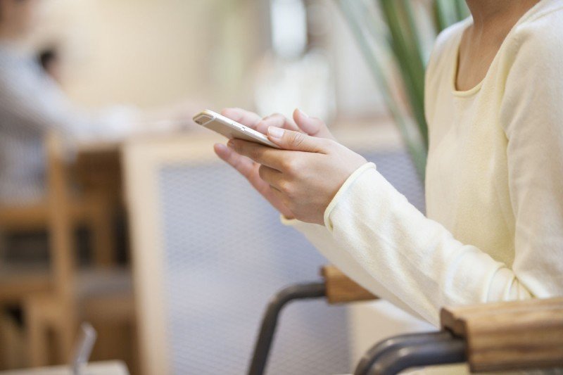 A woman's torso, arms, and hands are shown. She is holding a smart phone.