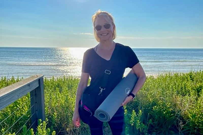 Kate Delp standing on the beach, smiling and holding a yoga mat