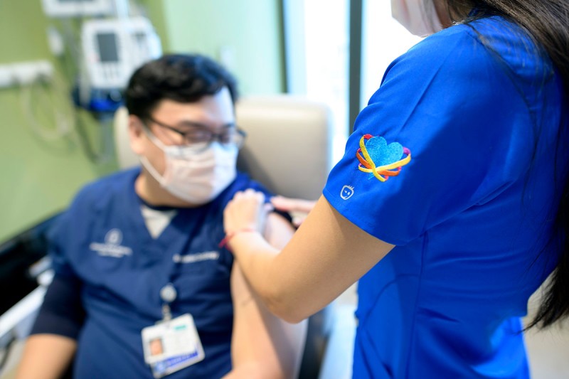 An MSK employee (seated) receives a COVID-19 vaccination.