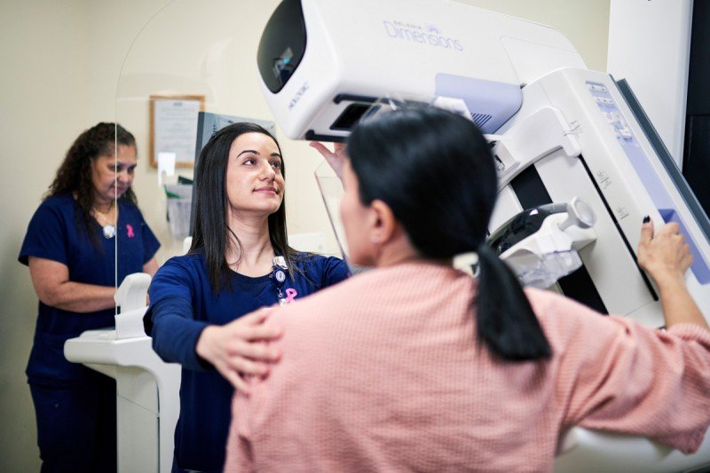 A technician using a 3D mammography machine on a patient