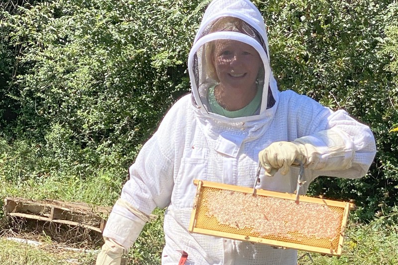 Woman in beekeeping protective outfit holding up honeycomb.