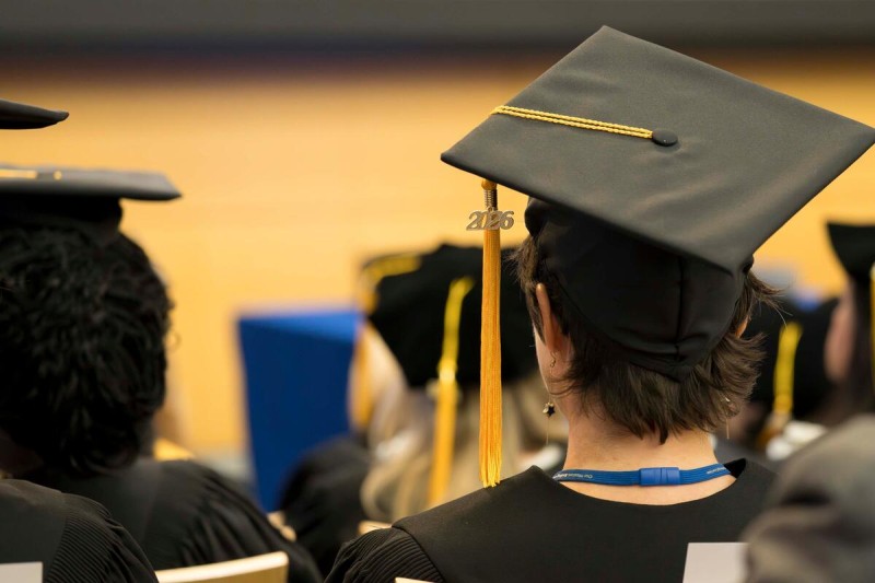 A row of seat graduates wearing their caps and gowns, shown from the back