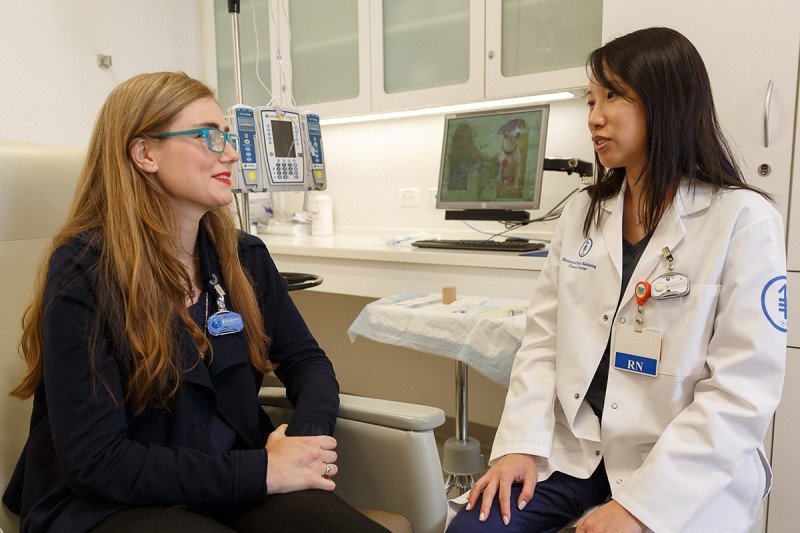 Nurse (seated in white coat on right) speaks with seated patient on left.