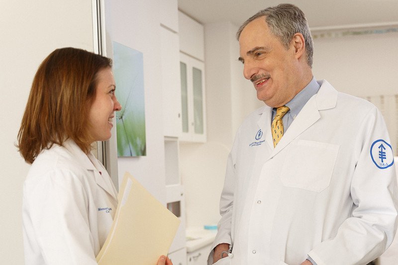 MSK hematologic oncologists, David Straus, dressed in a white coat speaks to a female nurse holding a folder.