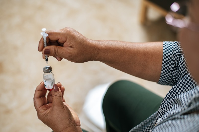 A person's hand holds a syringe, with its needle inserted into a vial of clear liquid