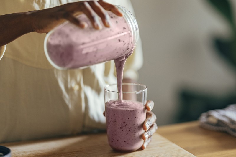 A pink smoothie is poured from a pitcher into a glass