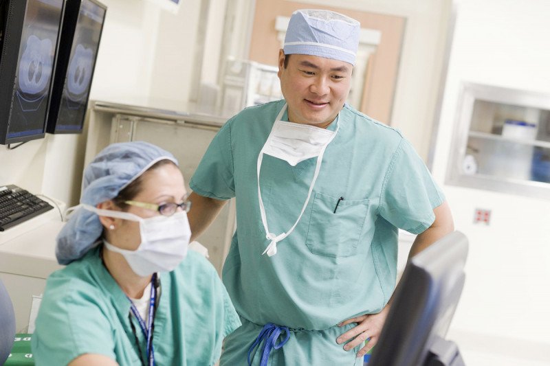 Thoracic surgeon James Huang stands and speaks to second oncologist sitting at a computer.