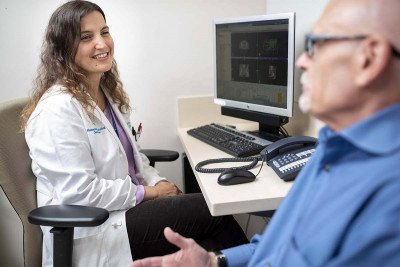 MSK radiation oncologist, Marisa Kollmeier, sits in front of a computer at her desk while speaking to a male patient.