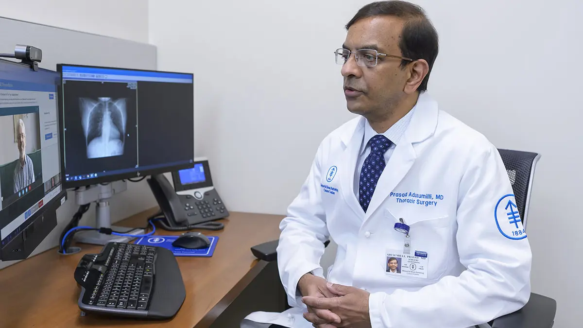 Dr. Prasad Adusumilli sits at a computer. A patient’s face and a chest image are on the screen.