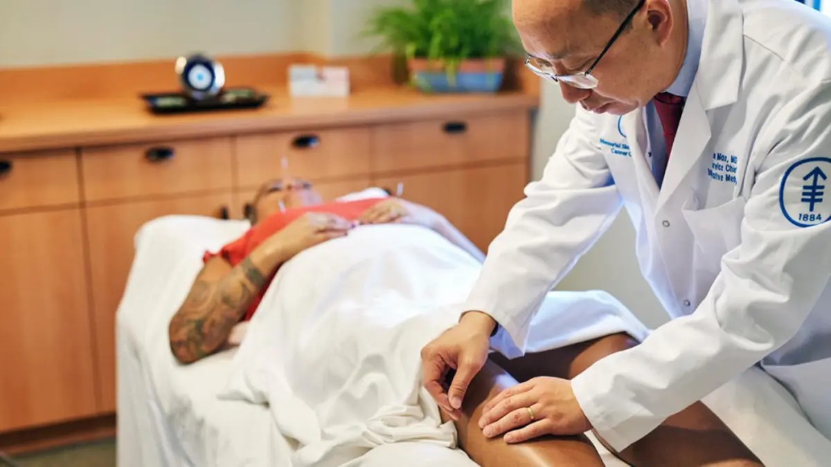 Dr. Jun Mao is treating an MSK patient, lying on a table, with acupuncture. 