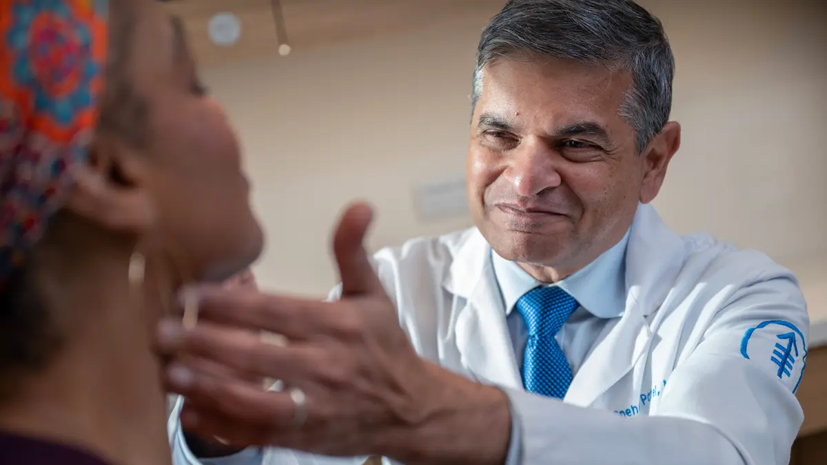 Head and neck surgeon Dr. Snehal Patel examines the neck of his patient in an exam room. 
