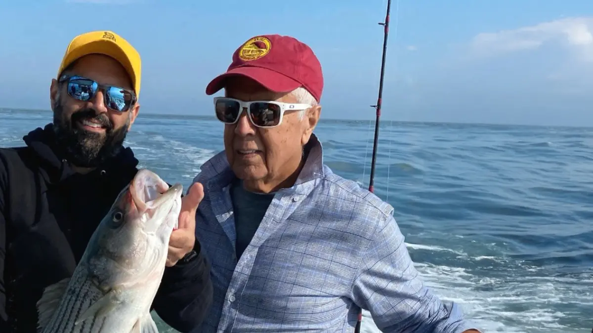 MSK patient Jack Georgakis wears a yellow baseball cap and sunglasses while holding a fish he’s just caught. His father, in a red hat and sunglasses, stands beside him, with the open ocean in the background.