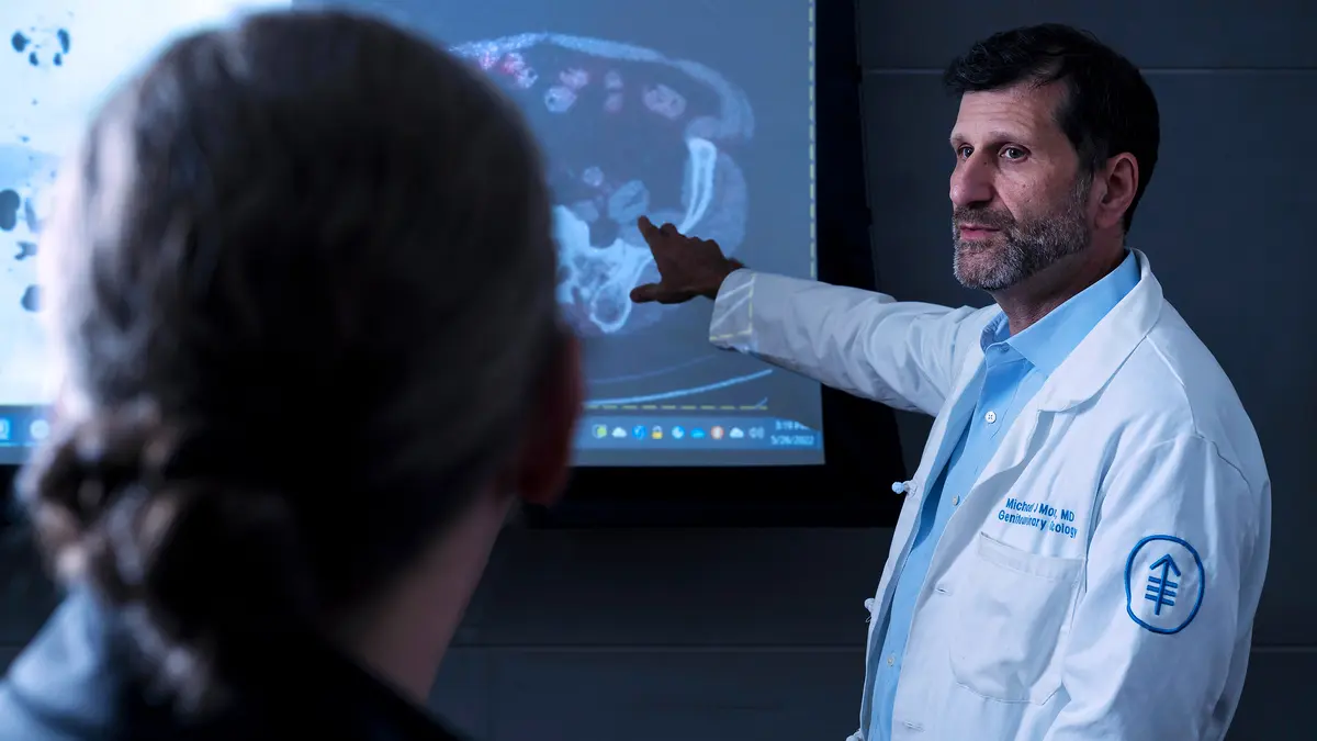 Medical oncologist Dr. Michael J. Morris points to a scan on a large monitor as he talks with his patient.  