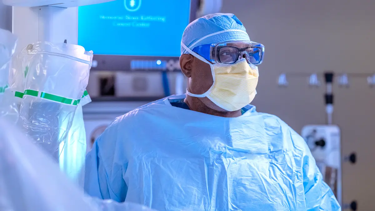 An MSK surgery team member, wearing surgical protective gear, is standing in a surgery suite during a robotic prostatectomy. 