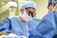 Surgeon in scrubs operating on patient.