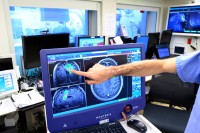 A hand points to brain images on a screen.
