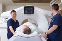 Two health care providers standing over a patient on a CT bed