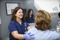 A woman receives a mammogram, and two technicians help her.