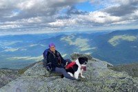 Elaine sitting down on a mountain with her border collie between her legs