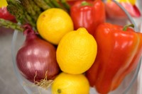 Bowl of lemons, onion, orange, and red peppers.