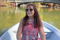 Ellen Coopersmith sitting in a row boat on the water with fall trees and a bridge in the background.
